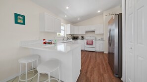 A modern kitchen with white cabinetry, a stainless steel refrigerator, and a wooden floor. - Gulf View Paradise - modern and spacious - Steps to beautiful Gulf Beach (Anna Maria)