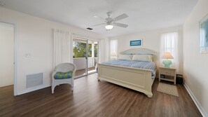 A bedroom with a bed, a chair, a ceiling fan, and a view through a glass door. - Gulf View Paradise - modern and spacious - Steps to beautiful Gulf Beach (Anna Maria)