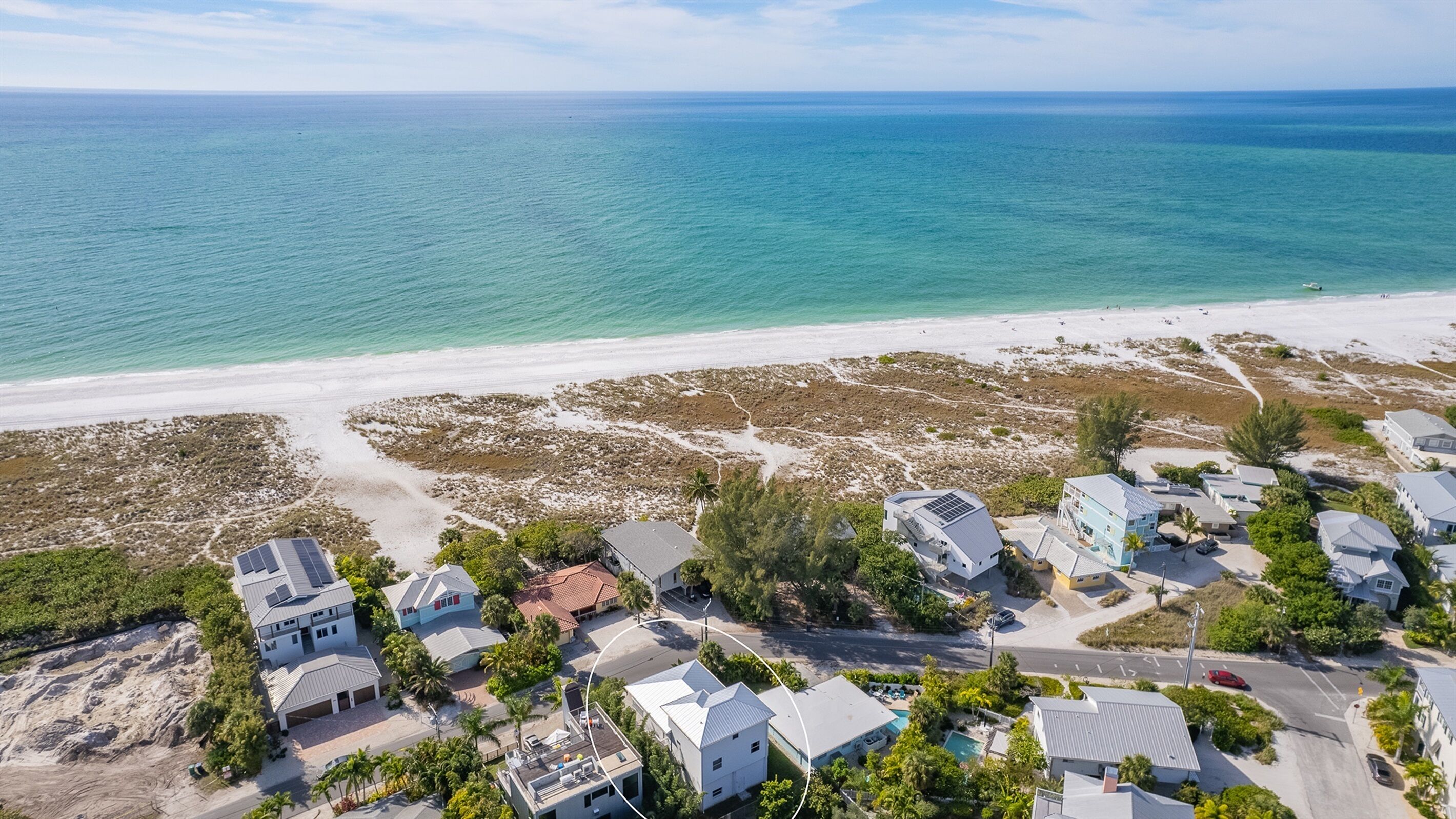 An aerial view of a coastal residential area with houses, a beach, and a clear view of the ocean.
