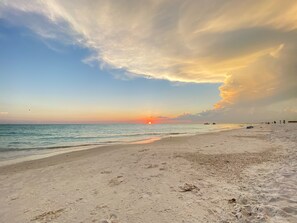 Una playa con huellas que conducen al agua, un bote y un atardecer.