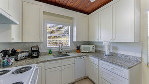 Una cocina con armarios blancos, microondas, tostadora y ventana con persianas.