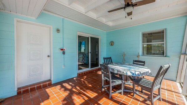 Une terrasse couverte avec une table et des chaises, une porte-fenêtre coulissante et un ventilateur de plafond.