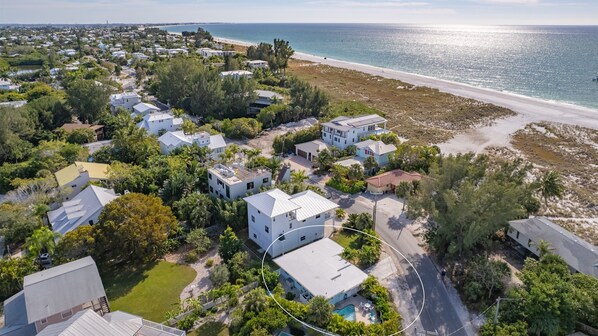 An aerial view of a coastal residential area with houses, a beach, and a clear sky.