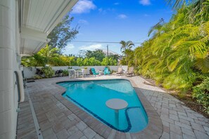 A swimming pool with a unique shape, surrounded by a paved patio and outdoor furniture.