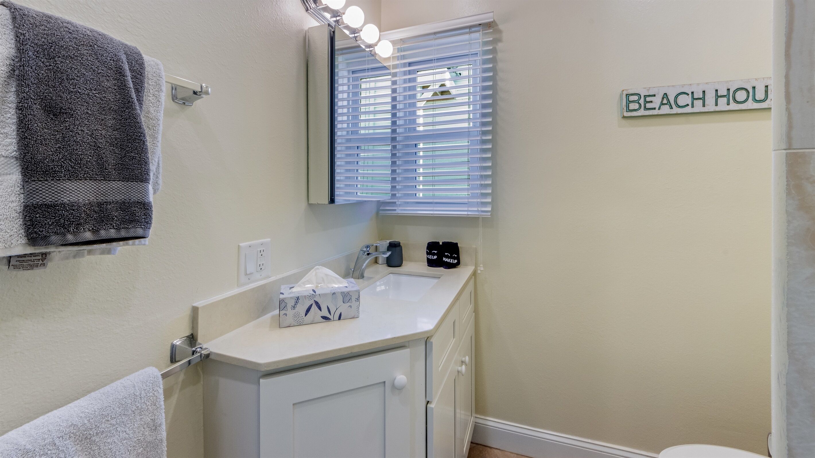 A bathroom with a sink, towel rack, and a sign that reads 'BEACH HOUSE'.