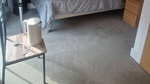 A bedroom with a bed, bedside table, lamp, and a chair. - Room-a Friendly Budget Room That Deliver (Southampton)