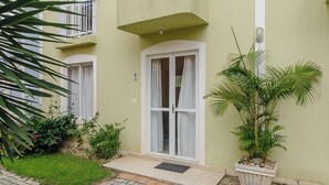 A building with a green exterior, a white door, and a small garden area with plants and a potted tree. - 2BR House w/ BBQ 150m From Beach Ccm0008 (Bombinhas)