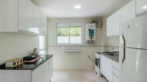 A compact kitchen with white cabinets, a window, a built-in water heater, and a refrigerator. - 2BR House w/ BBQ 150m From Beach Ccm0008 (Bombinhas)