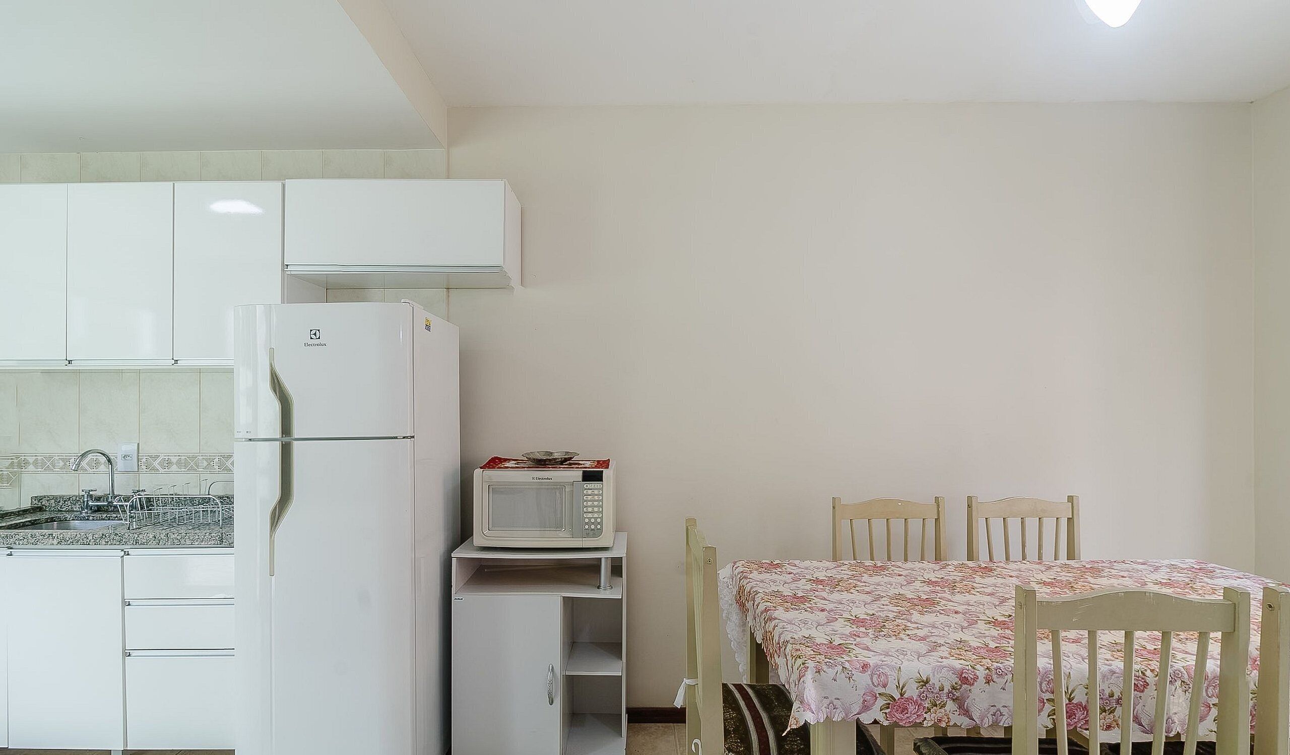 Una cocina con refrigerador, microondas y una mesa de comedor con sillas.