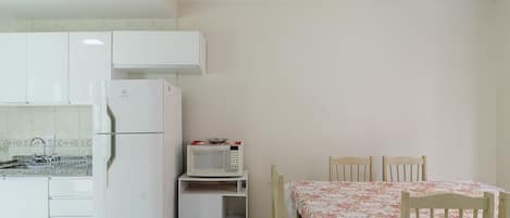 Una cocina con refrigerador, microondas y una mesa de comedor con sillas.
