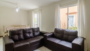 A living room with a dark brown leather sofa, a dining table with chairs, and a window with curtains. - 2BR House w/ BBQ 150m From Beach Ccm0008 (Bombinhas)