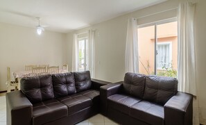 Ein Wohnzimmer mit einer dunkelbraunen Ledersofa, einem Esstisch mit Stühlen und einem Fenster mit Vorhängen.