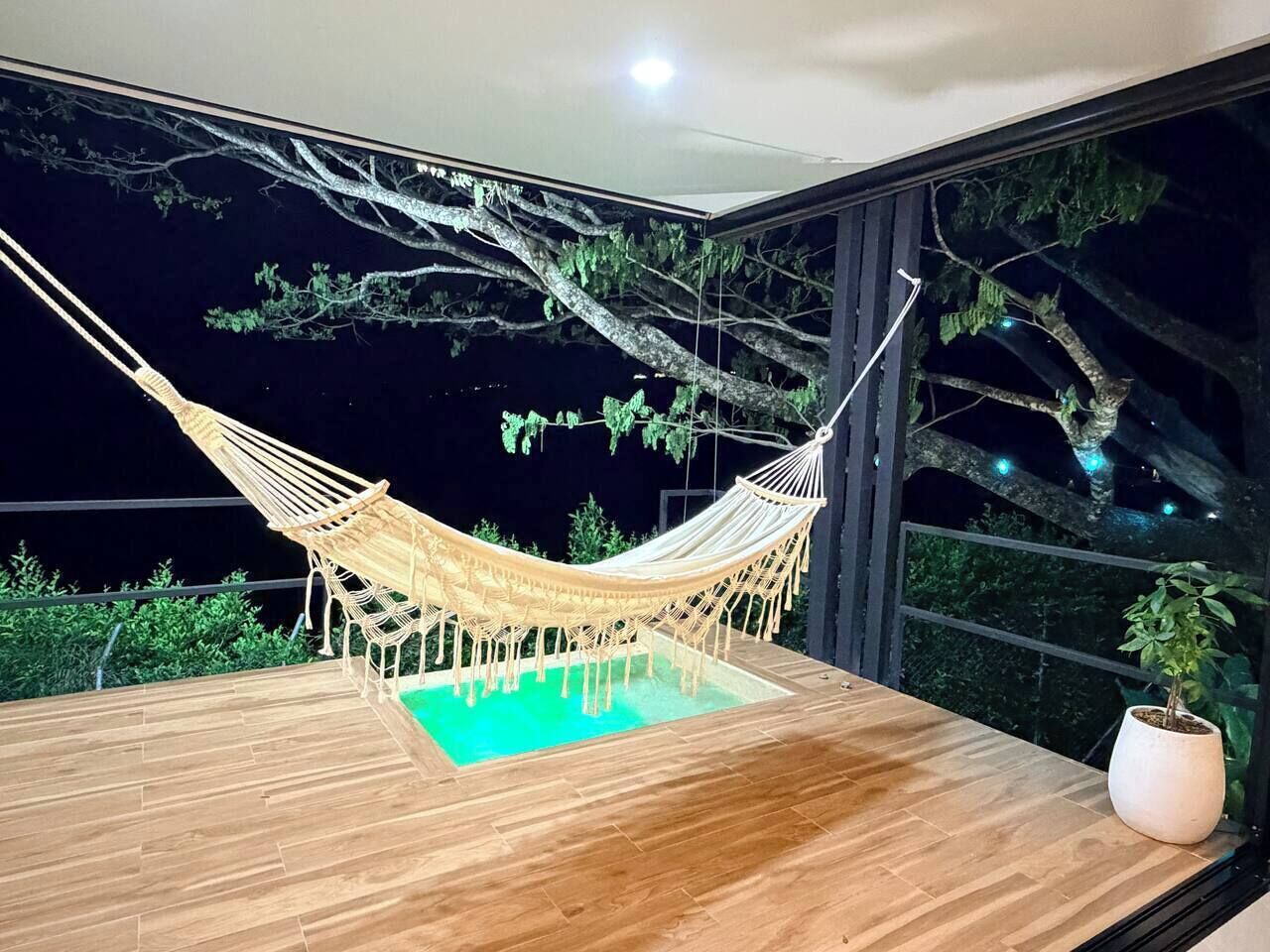 Una cadira lligadora sobre un pont de fusta amb una piscina, envoltada d'arbres i una planta en test.