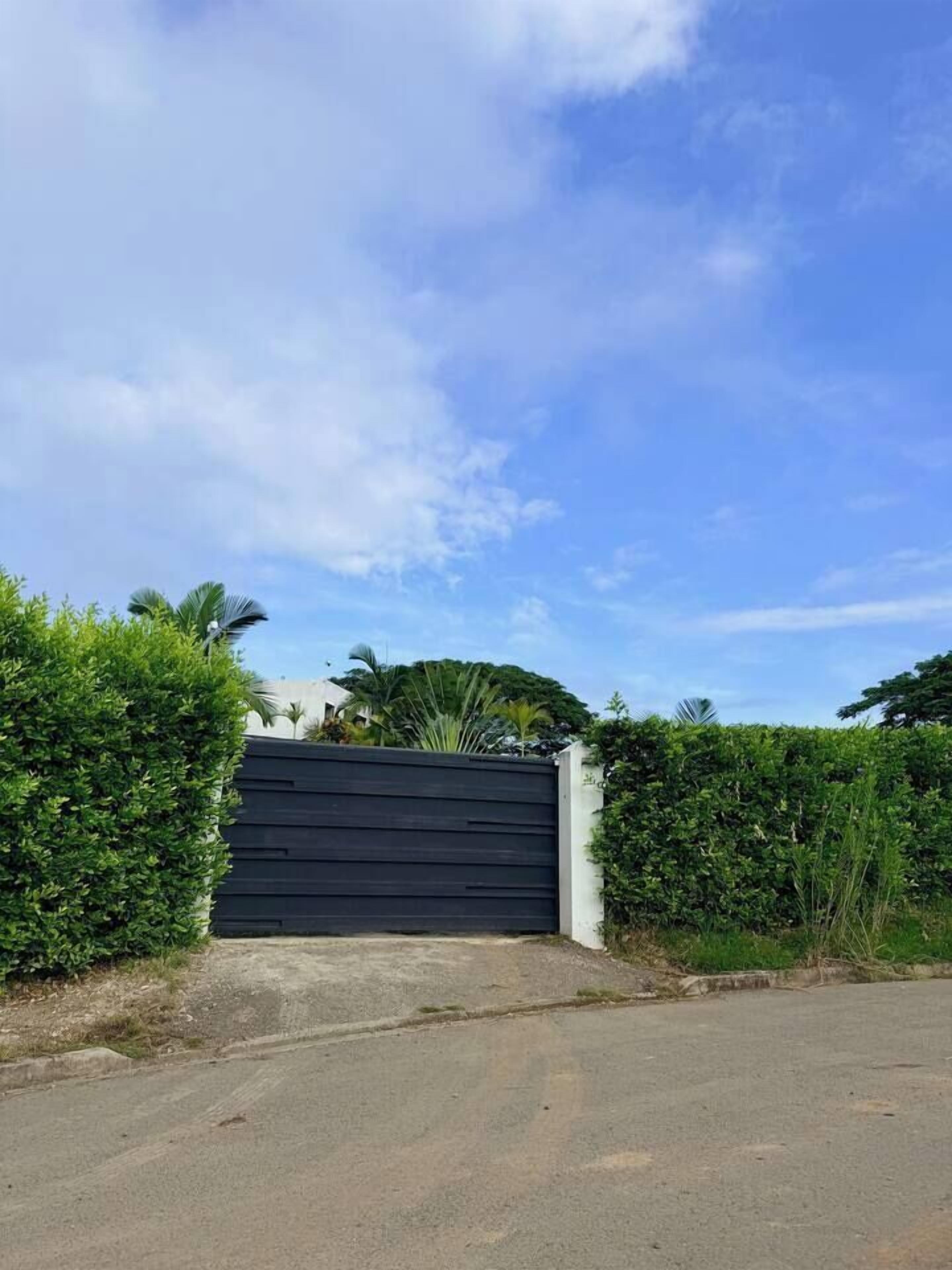 A gated driveway leading to a building with a modern design, surrounded by greenery.