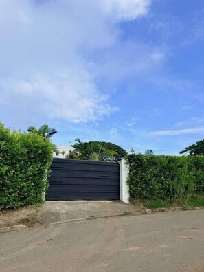 A gated driveway leading to a building with a modern design, surrounded by greenery.