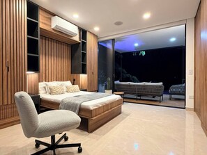 A modern bedroom with a large bed, a desk, and a balcony with seating.