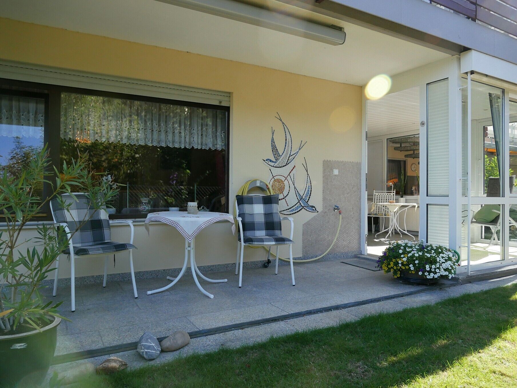 An outdoor patio with a table and chairs, a decorative wall piece, and a garden area with flowers.
