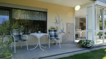 An outdoor patio with a table and chairs, a decorative wall piece, and a garden area with flowers.
