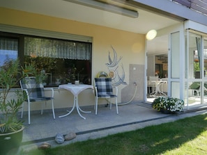 An outdoor patio with a table and chairs, a decorative wall piece, and a garden area with flowers. - Comfortable Holiday Apartment for 2 – Conservatory, Terrace, Lawn, Peace & Nature (Lauf)