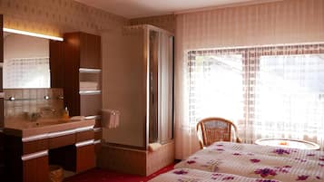 A hotel room with a bed, a chair, a bathroom with a sink, and a shower.