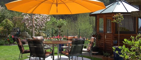Un patio con una mesa redonda, sillas, una sombrilla y una estructura de madera.