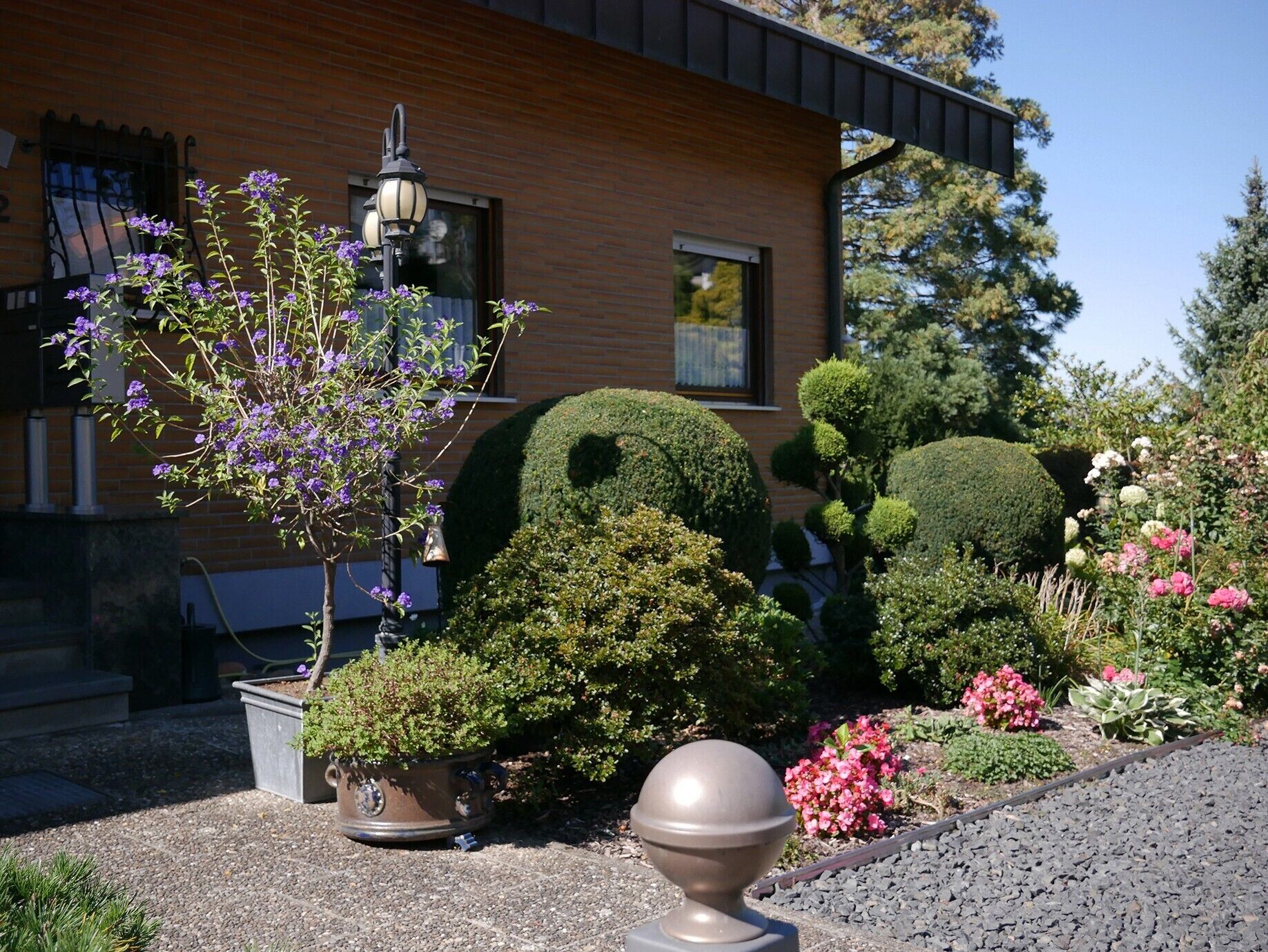 A building with a brick facade, a well-maintained garden with various plants and flowers, and a decorative lamp post.