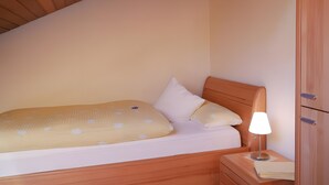 Ein Einzelbett mit Kopfstütze, ein Nachttisch mit Lampe und ein Holzschrank.
