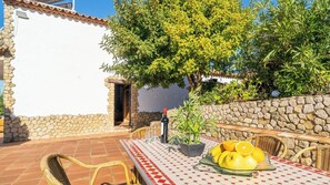 Eine Terrasse im Freien mit Esstisch, umgeben von Steinmauern und einem Baum, der Schatten spendet.
