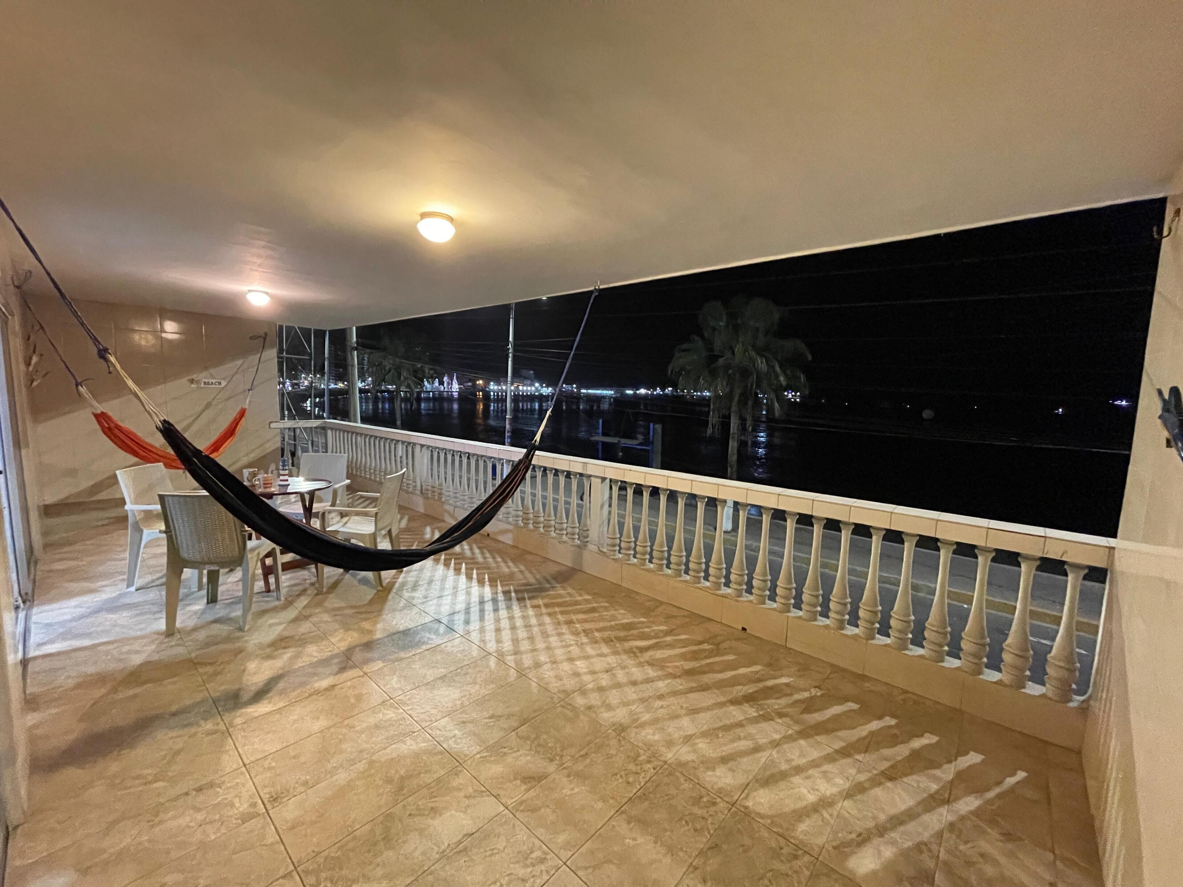 Un balcón con una hamaca, una mesa, sillas y vistas a la ciudad de noche.