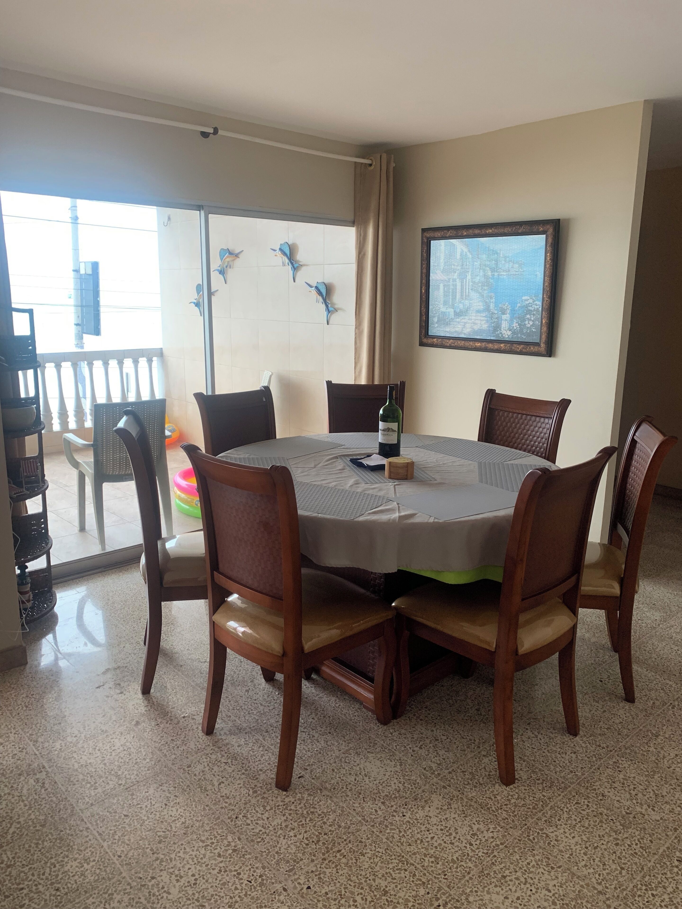 Un coin repas avec une table ronde, six chaises, une bouteille de vin et un tableau encadré accroché au mur.