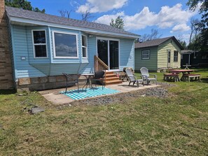 A single-story house with a porch, a set of stairs leading to the entrance, and a small outdoor seating area with chairs and a table. - The Reel Retreat - pontoon rental available  (Isanti)