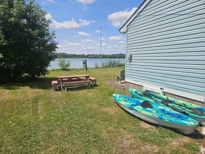 Eine Rasenfl äche mit Picknicktisch und Kajaks in der Nähe eines Gebäudes am See.