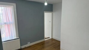 A room with a wooden floor, a radiator, a window with curtains, and a door. - Stunning Sea View Flat on The Leas Panoramic Estuary Sunsets, Steps to Beach (Sheerness)
