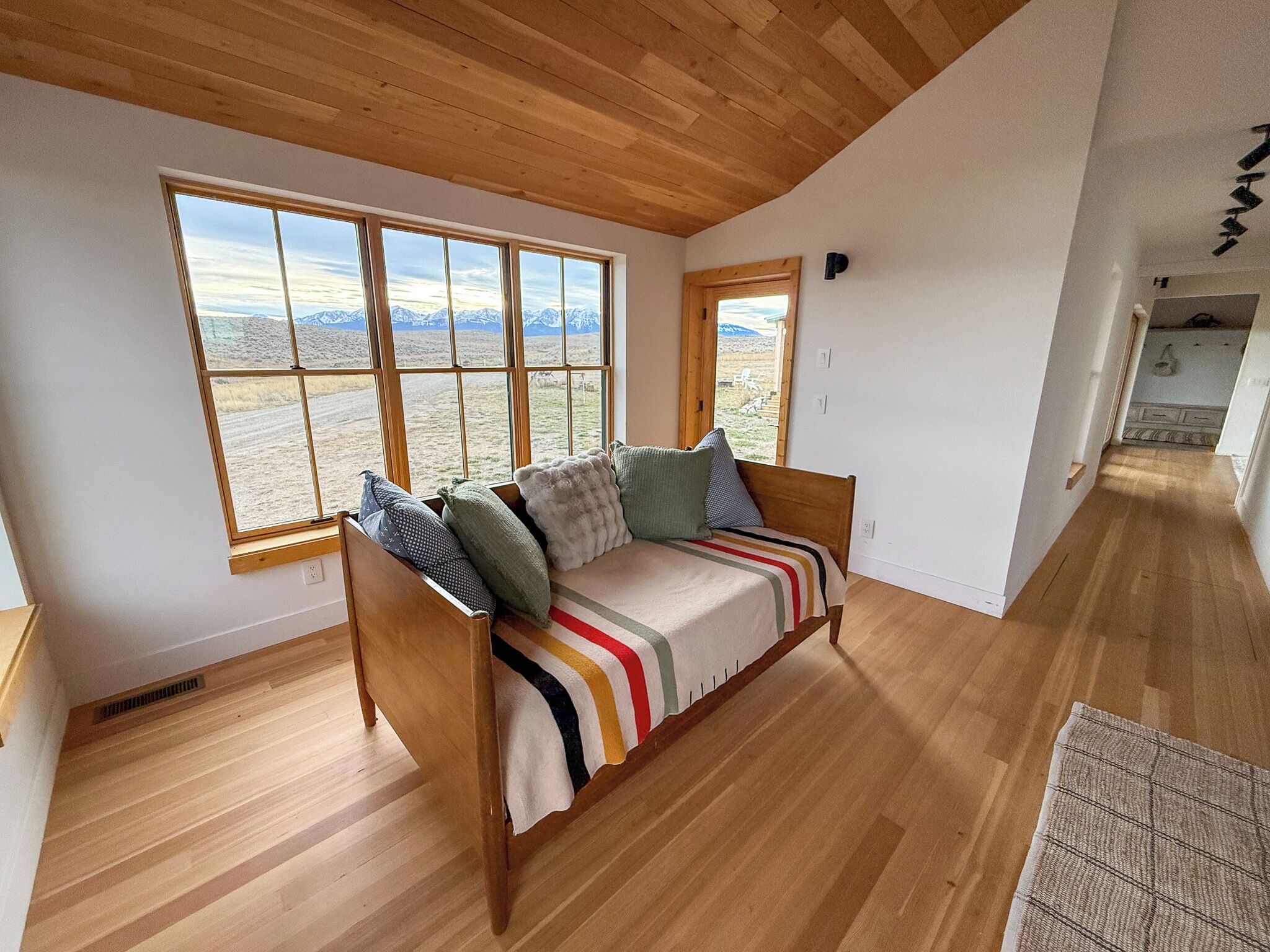 Ein Zimmer mit Holzboden, einem Sofa mit gestreiftem Überwurf und großen Fenstern mit Blick auf Berge.