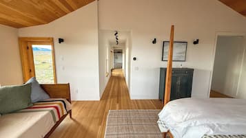 A bedroom with a wooden ceiling, a bed, a sofa, a desk, and a view of a landscape through a window.