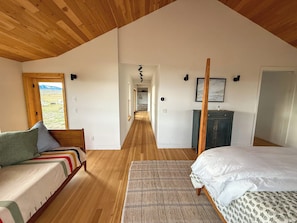 Un dormitorio con techo de madera, una cama, un sofá, un escritorio y vistas al paisaje a través de una ventana.