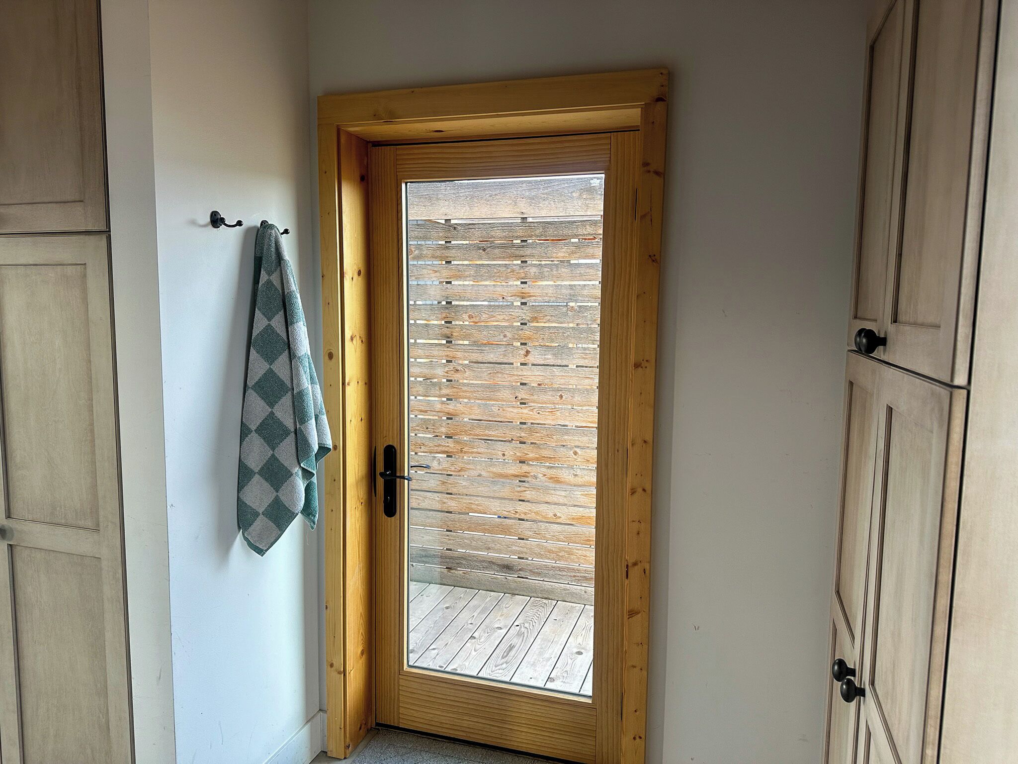 A wooden door with a glass panel, a towel hanging on a hook, and wooden flooring.