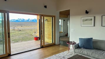 Ein modernes Wohnzimmer mit einem großen Schiebeglastür, die auf eine Terrasse führt, einem grauen Sofa, einem kleinen runden Tisch und einem Holztisch.