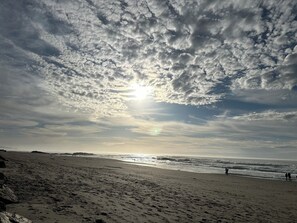 Ein Strand mit Fußabdrücken und Wellen, unter einem bewölkten Himmel.
