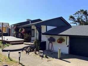 Ein Wohnhaus mit Garage und einer Veranda, die mit Blumentöpfen geschmückt ist, unter einem wolkenlosen Himmel.