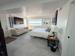 A bedroom with a bed, a sofa, a window with a view of the beach, a trash bin, and a door. - Breath taking ocean view in Lincoln City.  100 steps to the beach (Lincoln City)