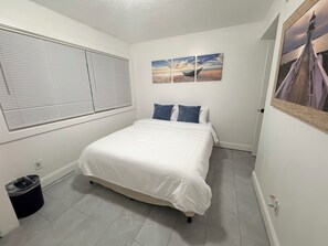 Un dormitorio con una cama, un ventanal con persianas y tres cuadros colgados en la pared.