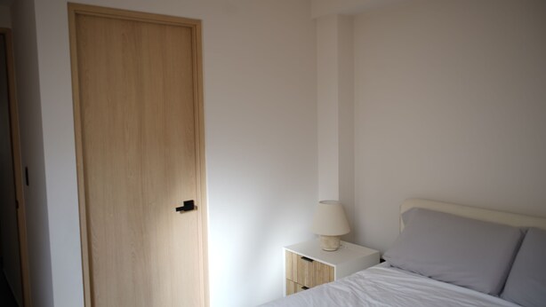 A bedroom with a wooden door, a bedside table with a lamp, and a bed with pillows. - Lovely 3 BDRM Apartment in Napoles, CDMX. (Ciudad de México)