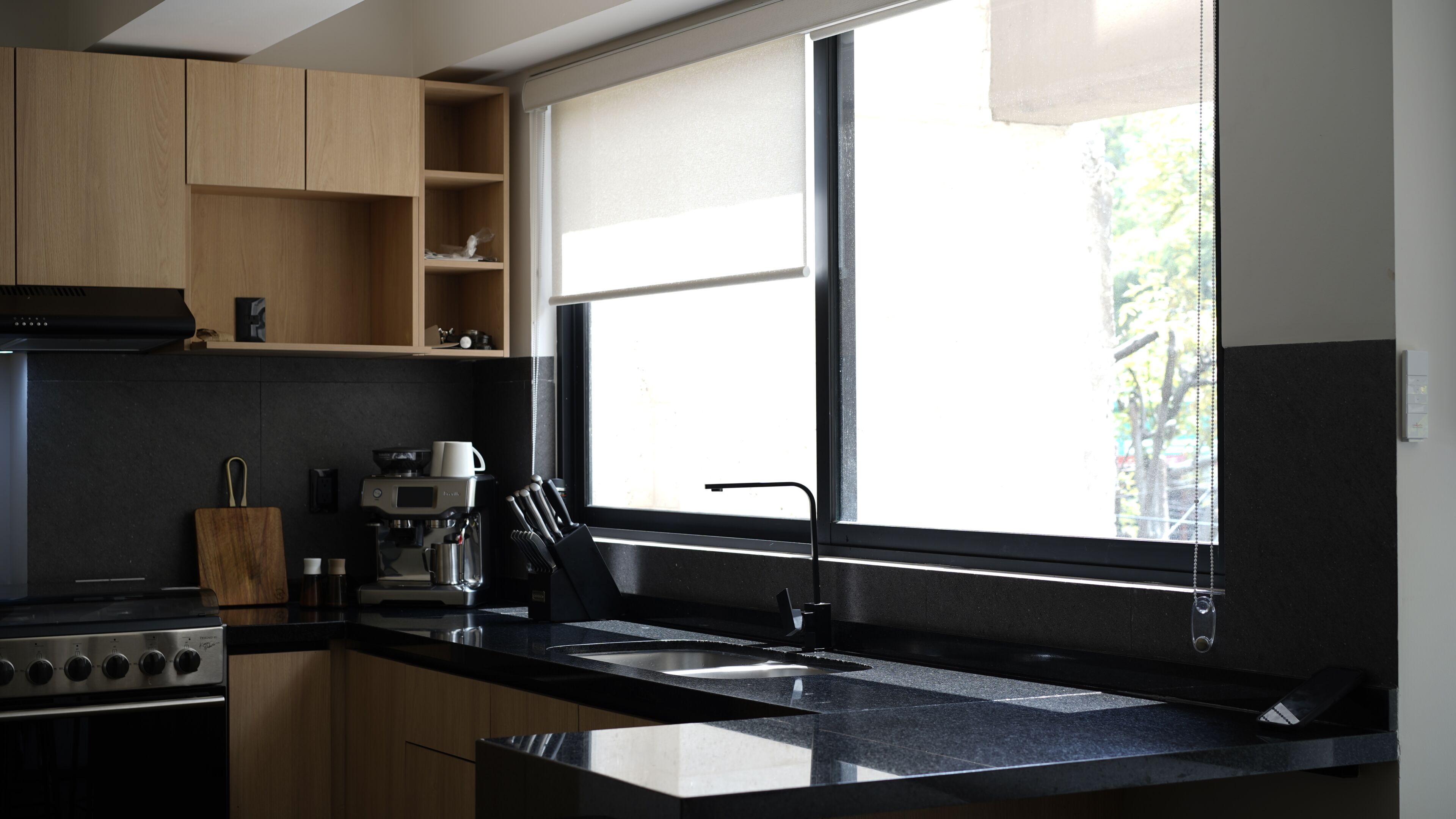 Una cucina moderna con un piano di lavoro nero, elettrodomestici in acciaio inossidabile e una finestra con persiane.