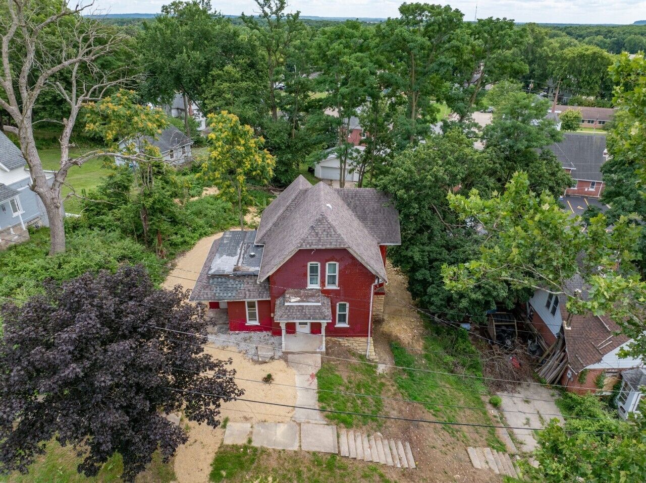 Una casa rossa con tetto grigio, circondata da alberi e un cielo sereno.