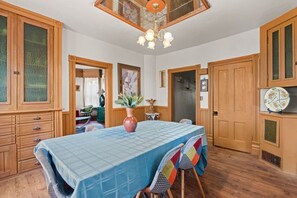 Ein Essbereich mit einem Tisch für vier Personen, Holzschränken, einer Chandelüster und Blick durch eine Tür.
