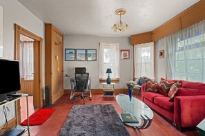 A living room with a red sofa, a glass coffee table, a TV, and a desk with a computer.