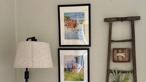 Eine Wand mit drei gerahmten Bildern, einer Stehlampe, einer Holzleiter und einem kleinen Topfpflanzen.