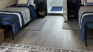 Ein Schlafzimmer mit zwei Betten, einer Deckenleuchte, einer Tür zu einem Badezimmer und einem gemusterten Teppich.