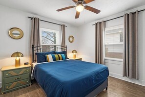 Un dormitorio con una cama, dos mesitas de noche, un ventilador de techo y una ventana con cortinas.